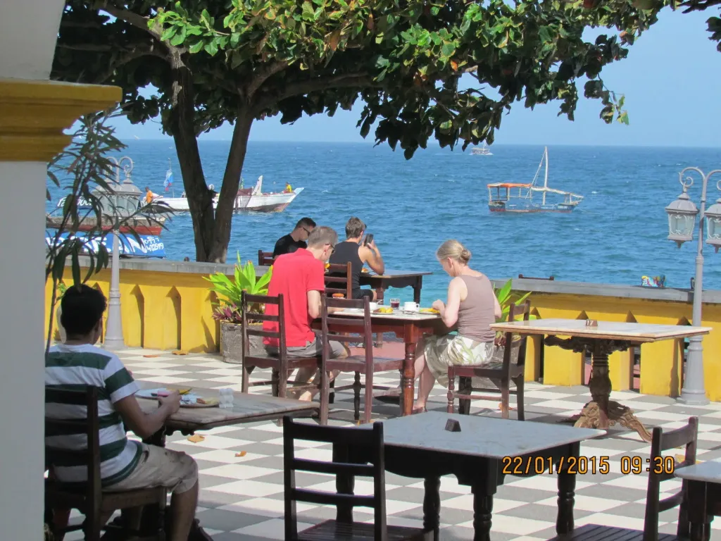 Des convives déjeunent à des tables en plein air face à la mer.