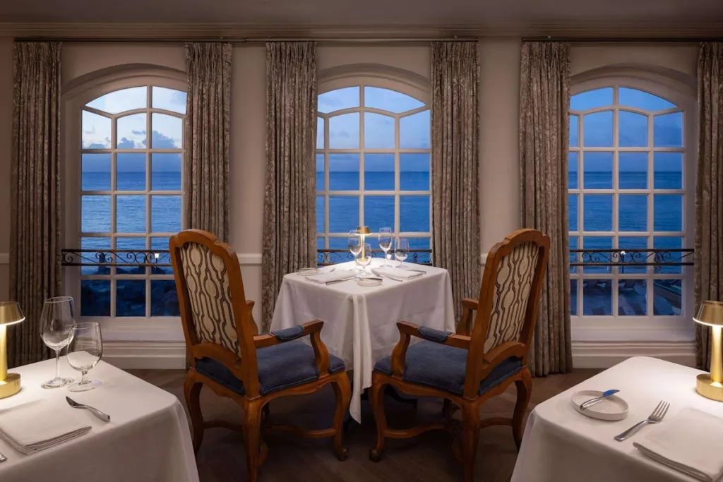 Tables dressées devant de larges fenêtres donnant sur la mer.