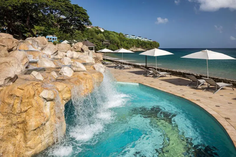 Une piscine avec cascade s'ouvre sur une plage de sable fin.