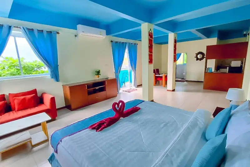 Une chambre lumineuse avec un lit décoré de serviettes en forme de cœur et un coin salon.