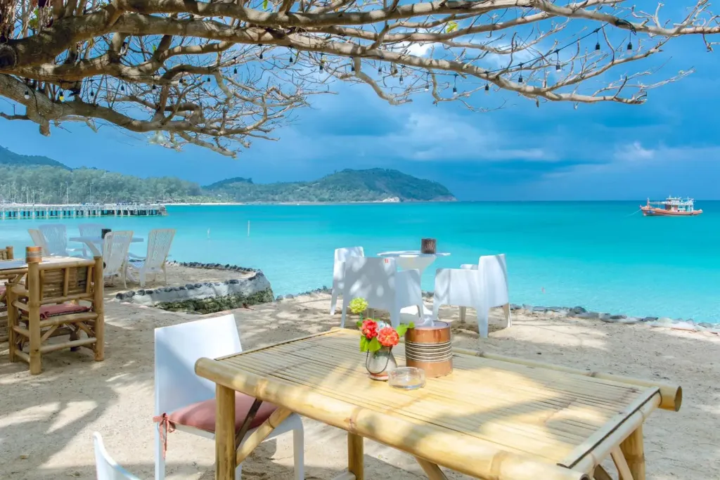Tables et chaises disposées sur une plage de sable fin face à la mer turquoise.