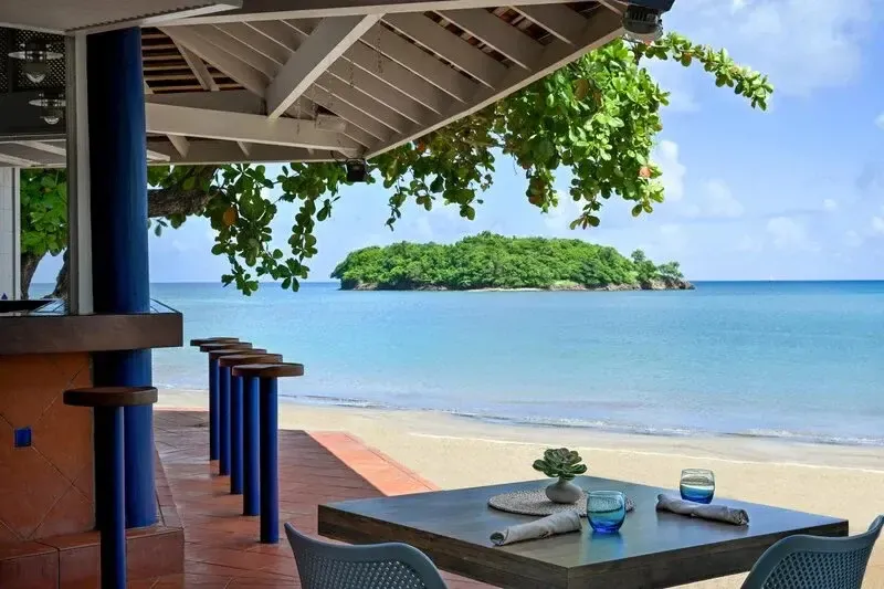 Une terrasse ombragée offre une vue sur une plage de sable fin et une île verdoyante.