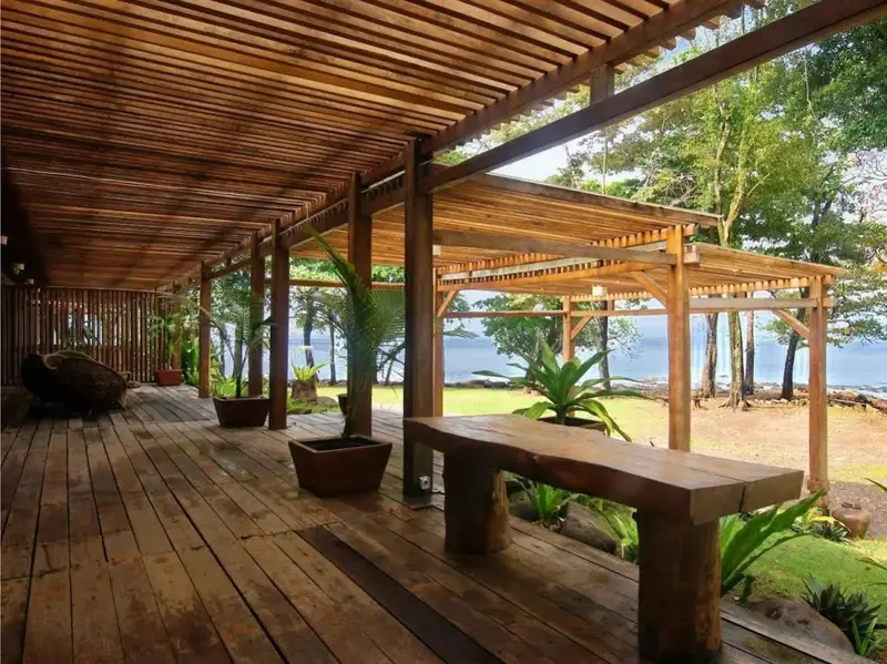 Terrasse en bois abritée avec mobilier rustique donnant sur un jardin tropical et la mer.