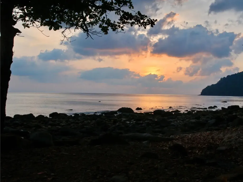 Coucher de soleil sur une plage rocheuse avec une mer calme.