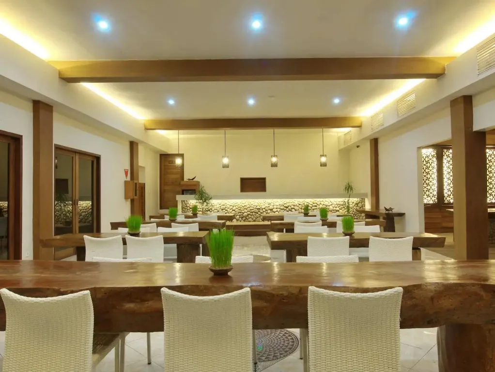 Une salle lumineuse avec de longues tables en bois et des chaises blanches.
