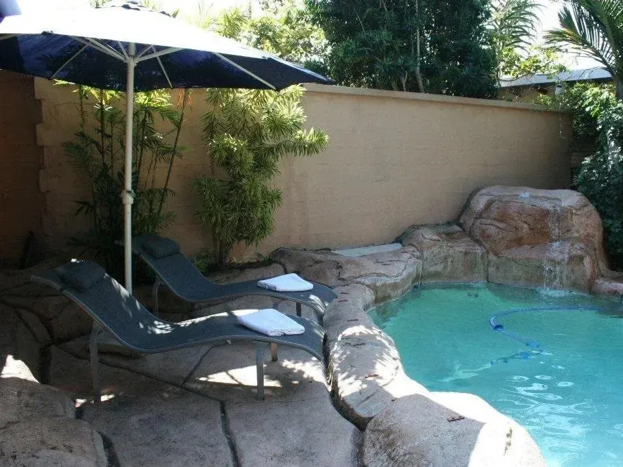 Deux transats avec serviettes sont placés près d'une piscine rocheuse et d'une végétation luxuriante.