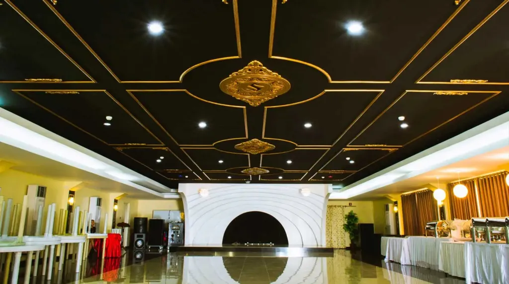 Grande salle lumineuse au plafond orné de motifs décoratifs.