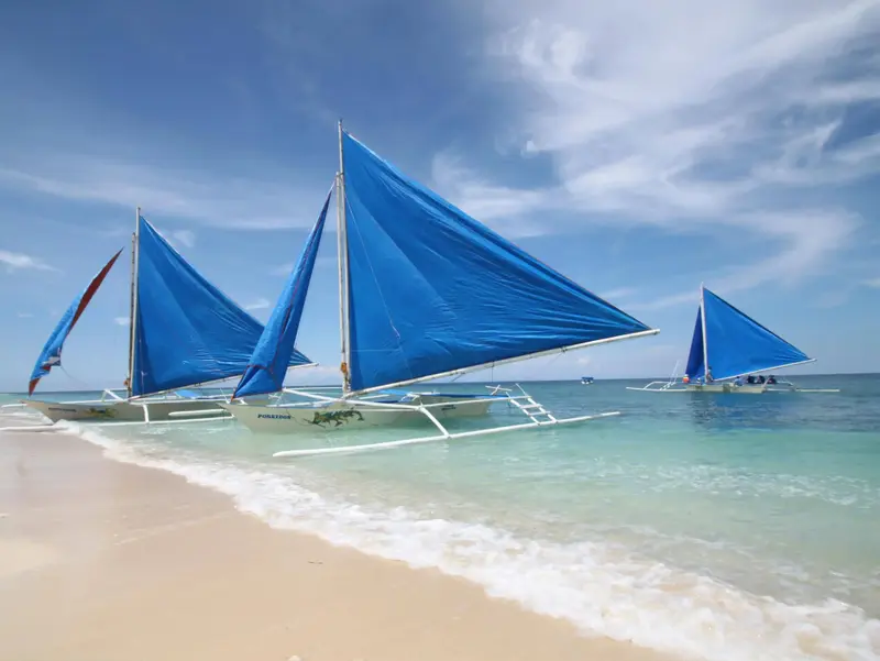Des voiliers échoués sur une plage de sable blanc sous un ciel bleu nuageux.