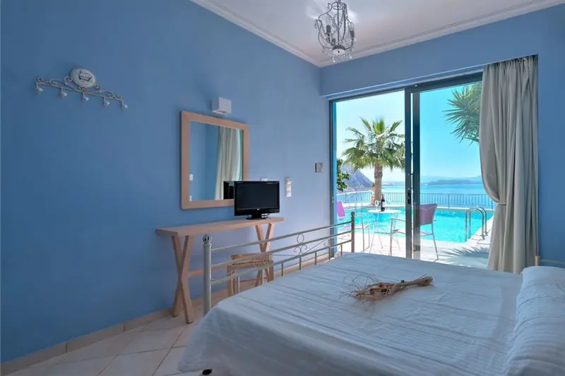 Une chambre lumineuse avec un lit blanc donnant sur une piscine et la mer.