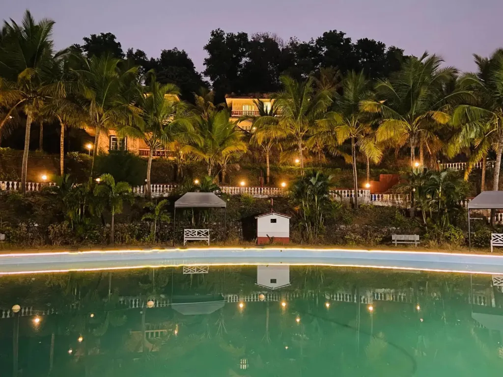 Une piscine illuminée reflète des bâtiments et des palmiers au crépuscule.
