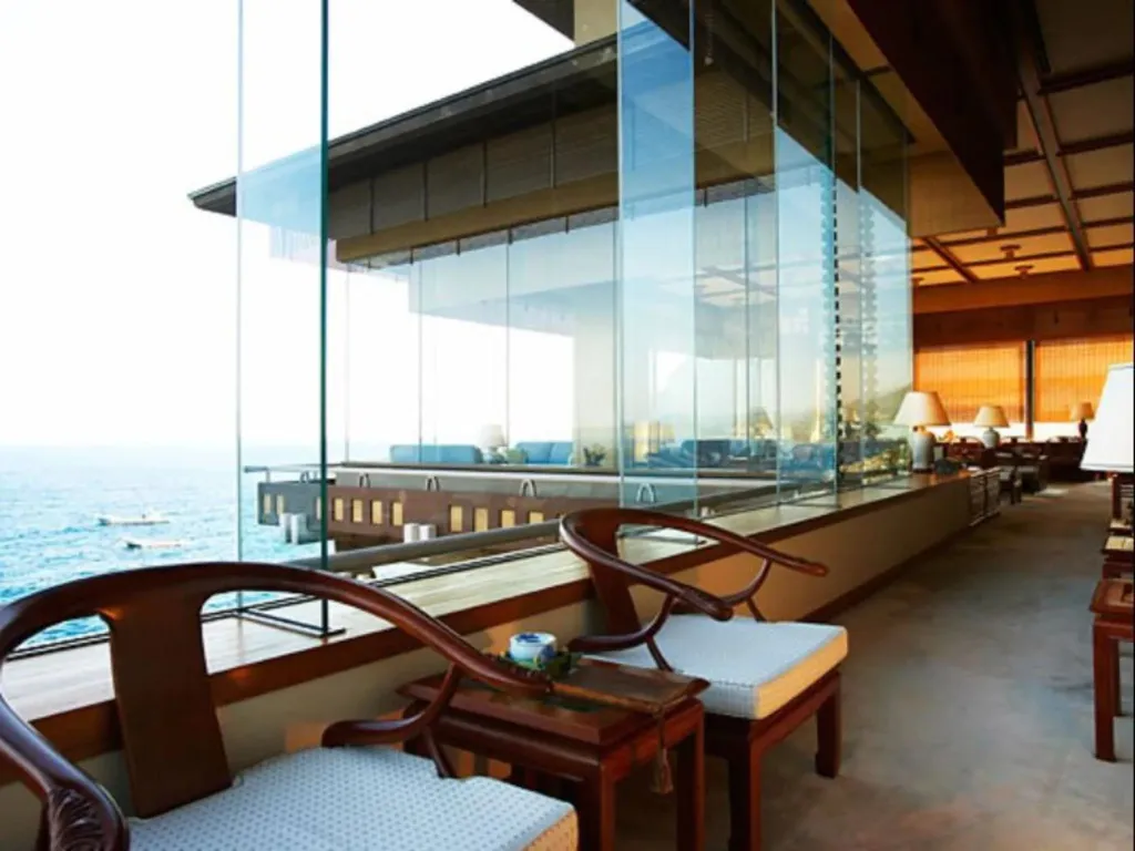 Espace de détente intérieur avec vue sur la mer à travers de grandes baies vitrées.