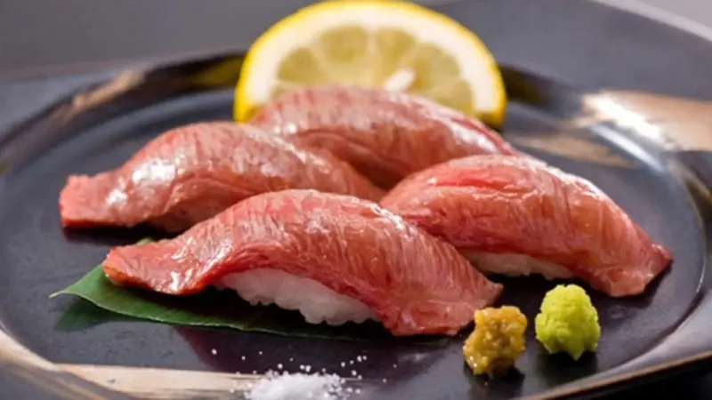 Quatre pièces de sushi au thon cru sont présentées sur une assiette noire avec une tranche de citron et une portion de wasabi.