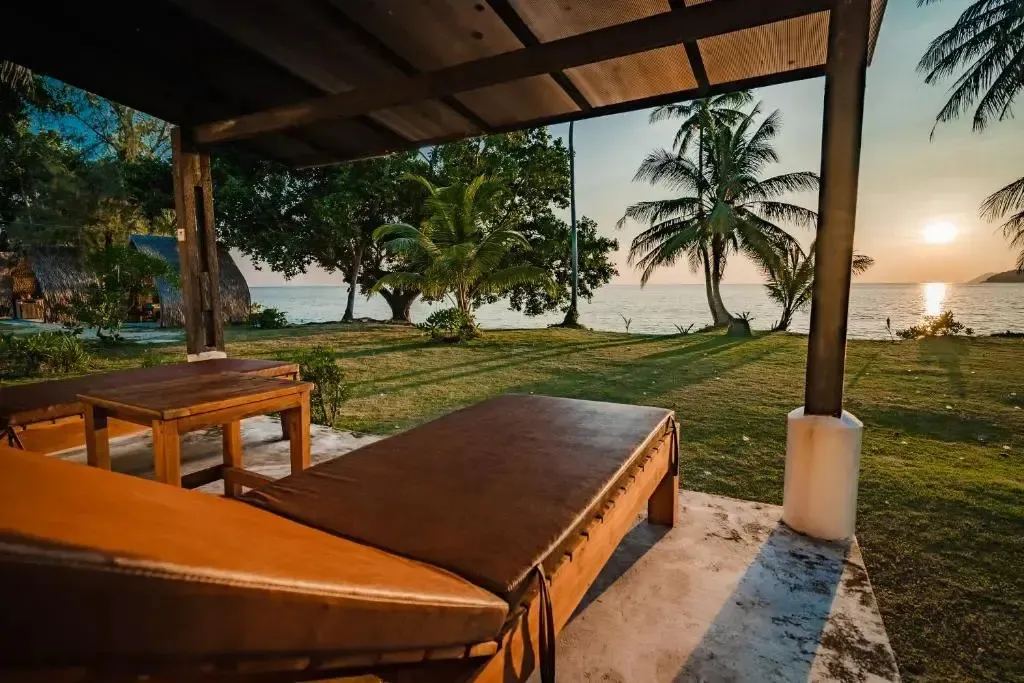 Terrasse avec mobilier de détente donnant sur une plage au coucher du soleil.