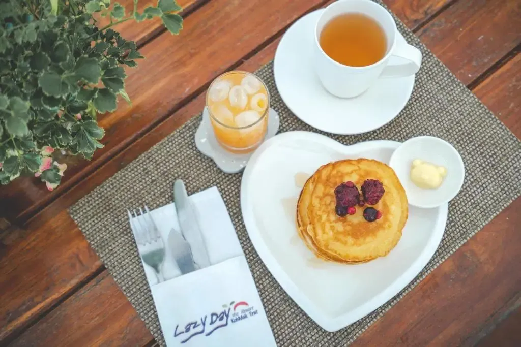 Une table en bois présente un petit-déjeuner avec des crêpes, des fruits et des boissons.
