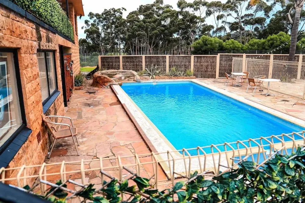 Une piscine rectangulaire est entourée d'une terrasse pavée et de végétation.