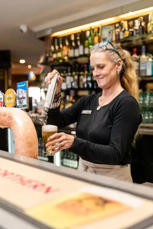 Une serveuse tire une bière à la pression dans un bar bien garni.