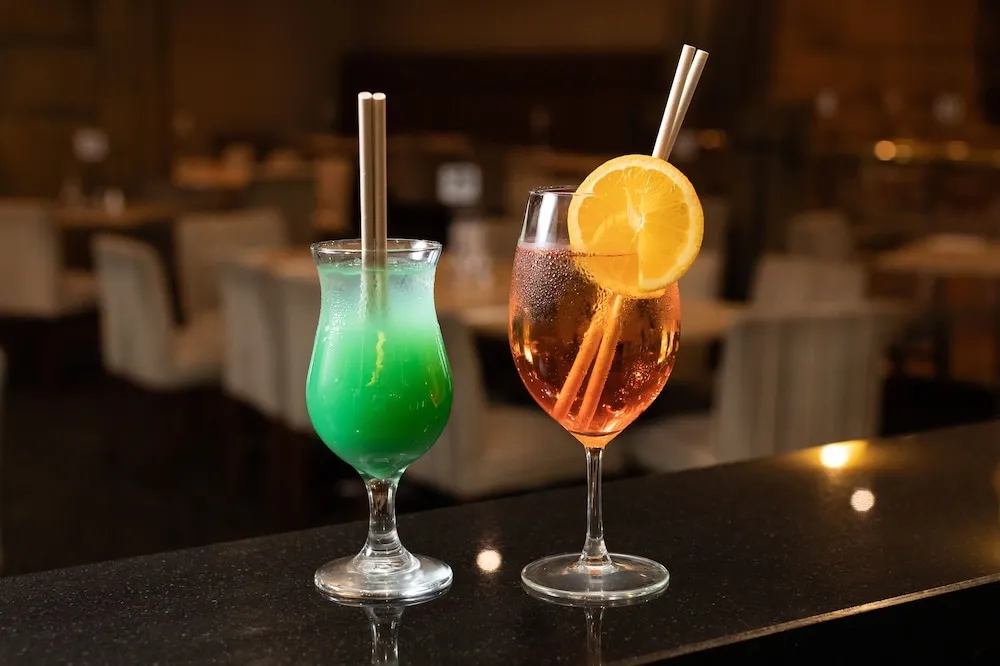 Deux cocktails colorés sont présentés sur un comptoir sombre.