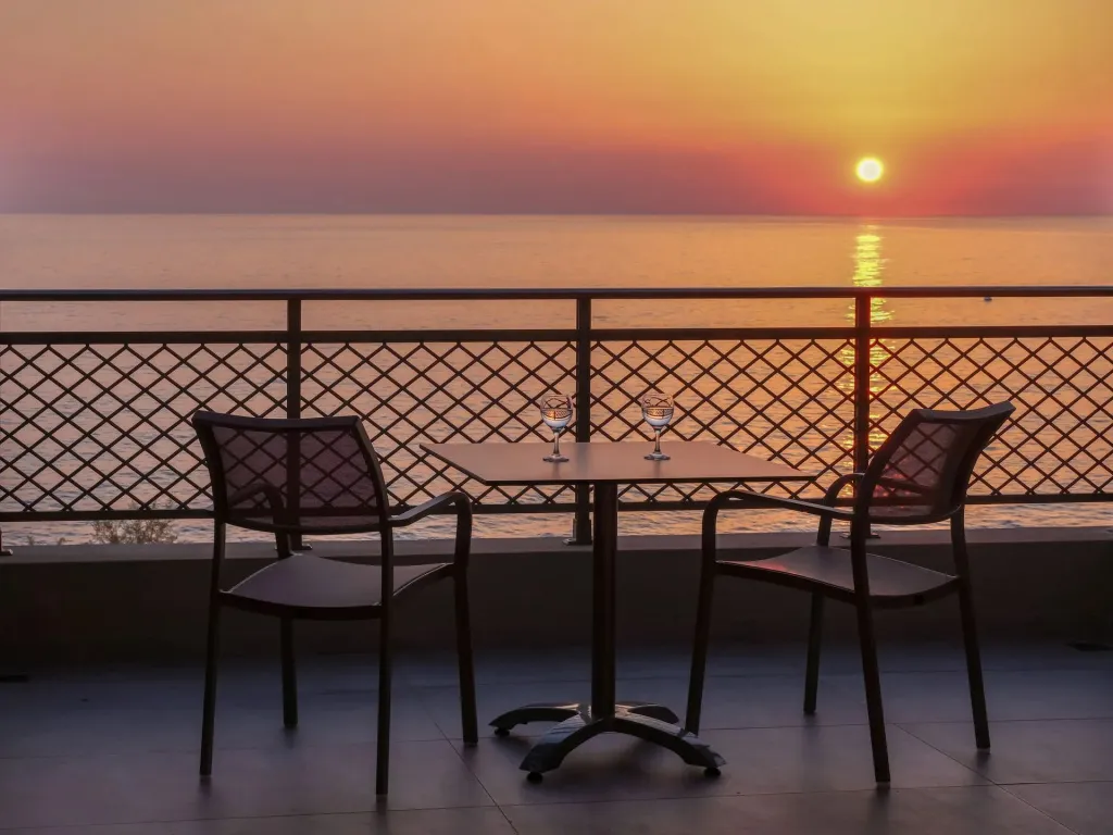 Une table et deux chaises sont disposées sur une terrasse face à la mer au coucher du soleil.