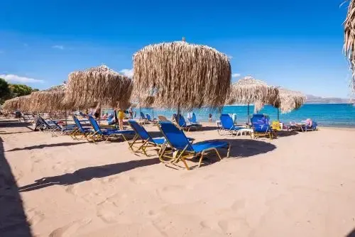 Transats et parasols de paille sur une plage de sable fin, bordée par une mer turquoise.