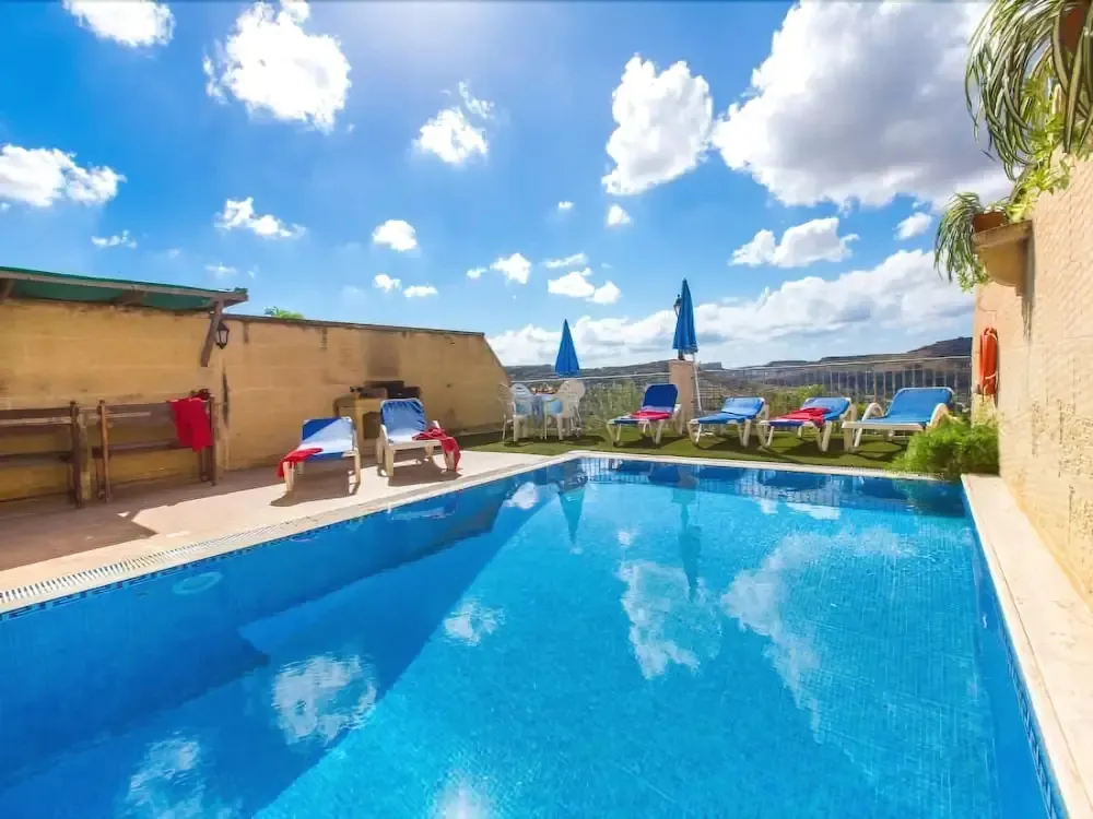 Une piscine rectangulaire avec des transats et des parasols sous un ciel bleu nuageux.