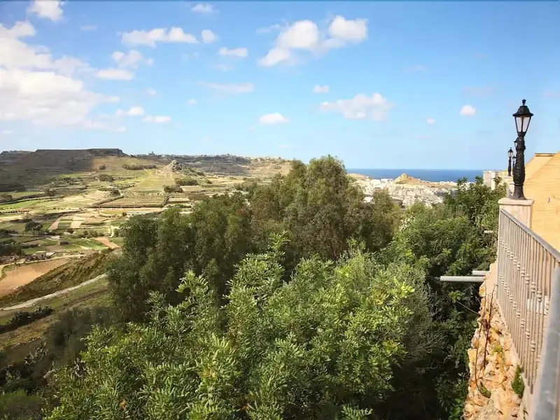 Vue panoramique sur une vallée verdoyante et la mer au loin.
