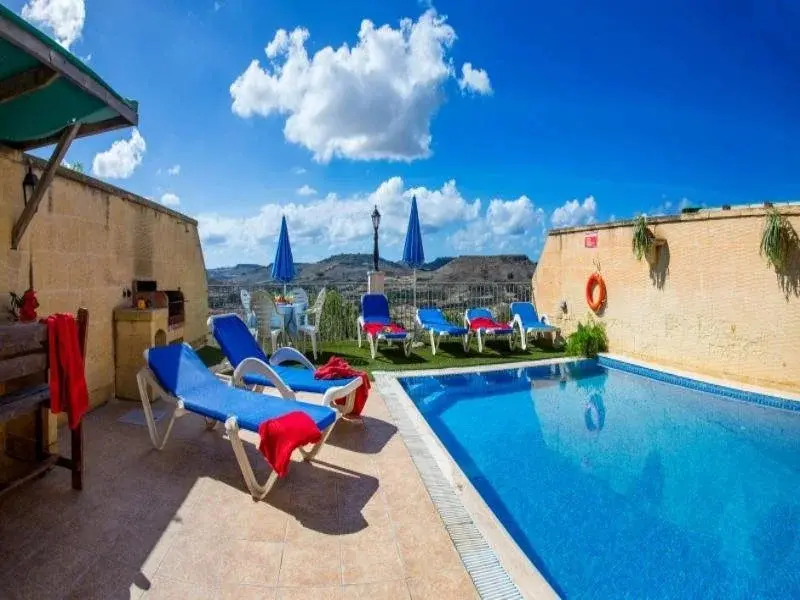 Transats bleus disposés autour d'une piscine ensoleillée avec vue sur un paysage montagneux.