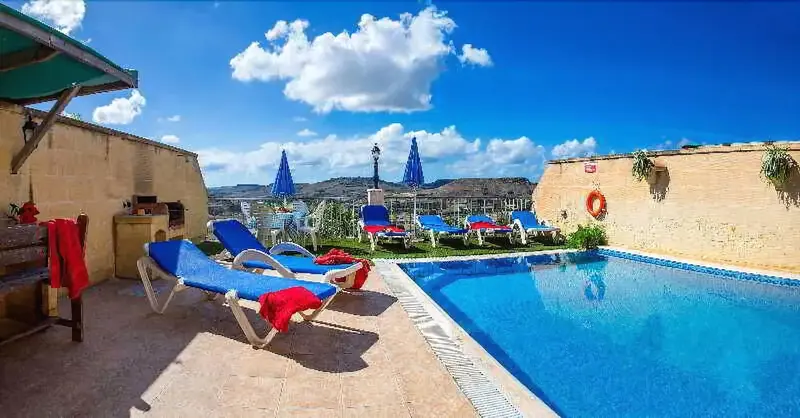 Transats bleus et rouges disposés autour d'une piscine ensoleillée avec vue sur un paysage montagneux.