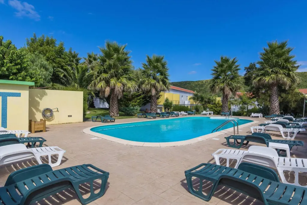 Une piscine ensoleillée avec des transats et des palmiers en arrière-plan.