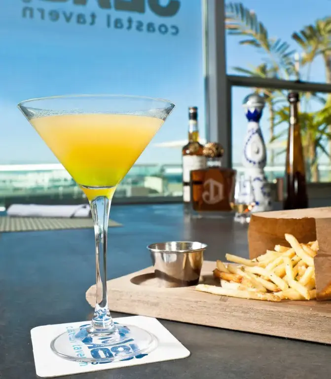 Un cocktail coloré et des amuse-gueules sont servis sur une table sombre.