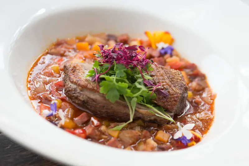 Un plat de viande servi dans une sauce colorée, agrémenté de jeunes pousses et de fleurs comestibles.