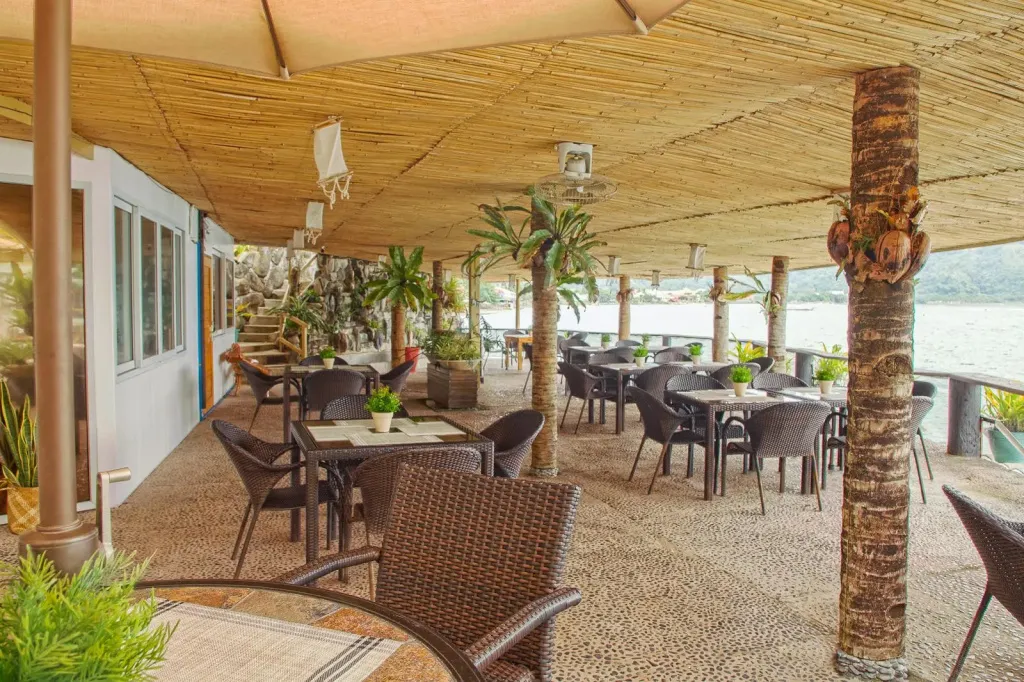 Une salle à manger extérieure ombragée avec des tables et des chaises en osier.