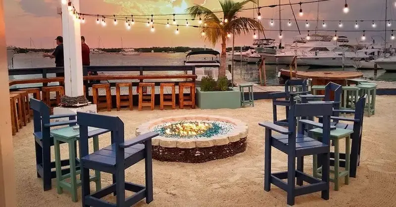 Espace de détente extérieur avec mobilier coloré et foyer central au bord de l'eau.