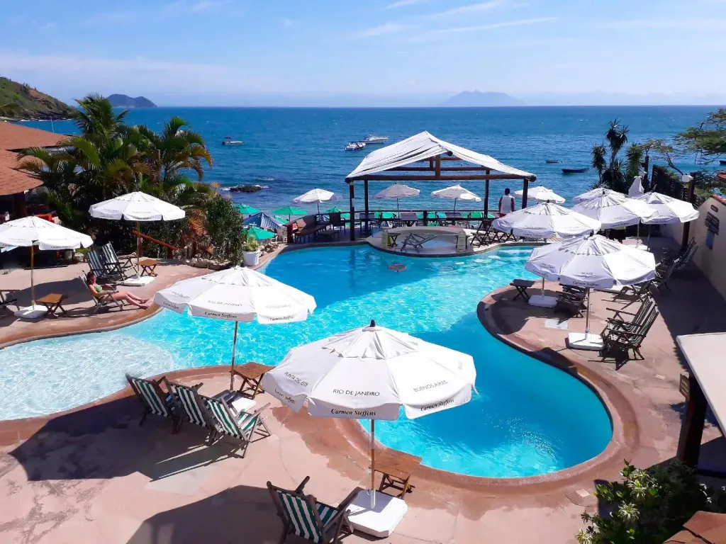 Piscine sinueuse avec parasols et espace détente ombragé en bord de mer.
