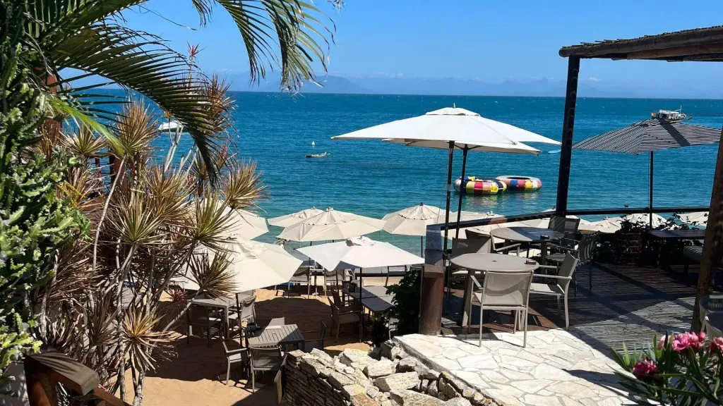 Terrasse ombragée avec tables et chaises donnant sur la mer.