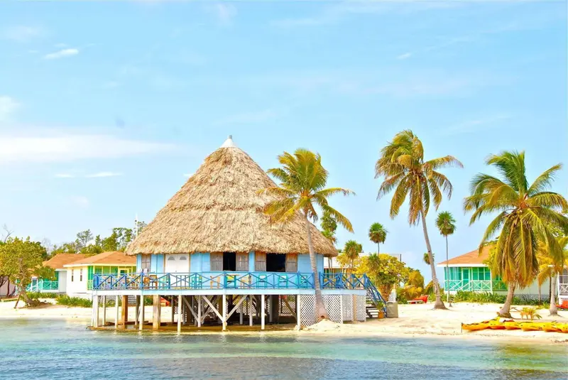 Bâtiment sur pilotis avec toiture de chaume surplombant une plage tropicale.