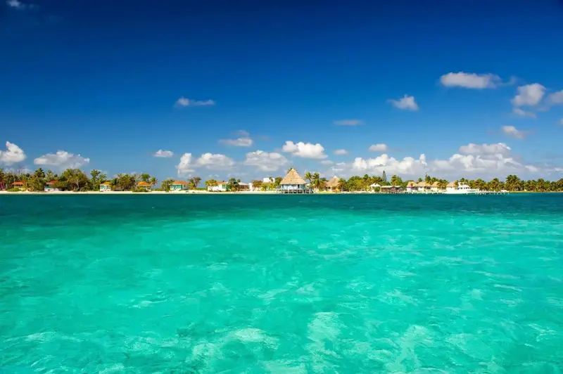 Vue sur une plage de sable blanc bordée de bâtiments aux toits de chaume sous un ciel bleu.