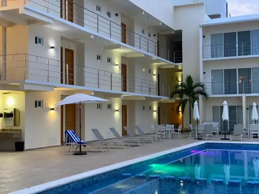 Une piscine éclairée devant un bâtiment à plusieurs étages avec des transats.