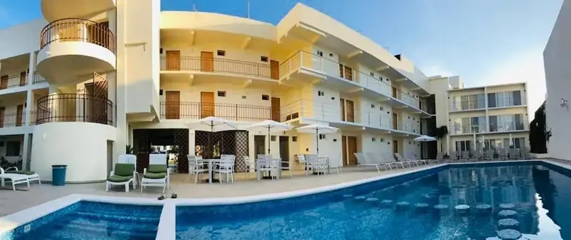 Vue d'un bâtiment blanc avec des balcons et une piscine au premier plan.