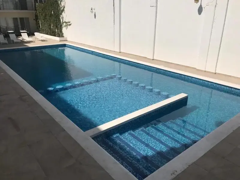 Une piscine rectangulaire avec des marches intégrées et un dallage clair.