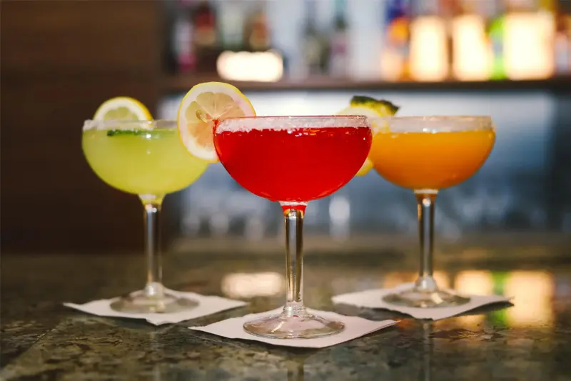 Trois cocktails colorés sont présentés sur un comptoir.