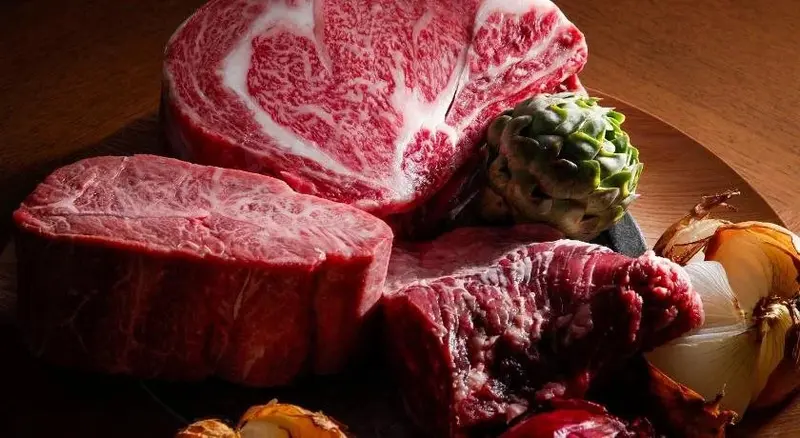 Des morceaux de viande crue sont présentés avec des légumes sur une planche à découper.