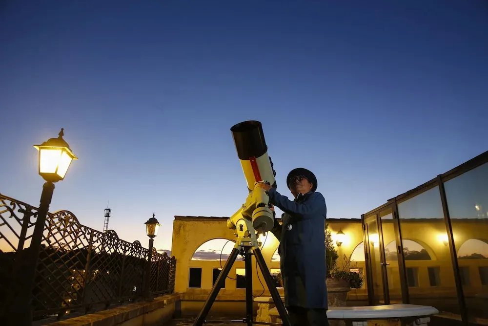 Une personne observe le ciel étoilé à travers un télescope sur une terrasse.