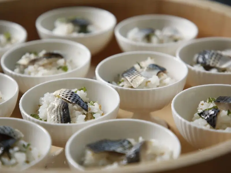 Petites portions de riz et de poisson disposées en rangées sur un plateau.