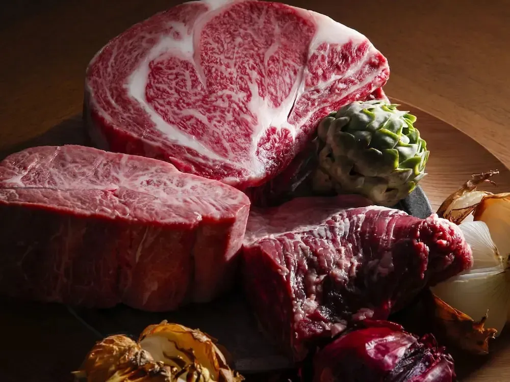Présentation de morceaux de viande rouge et d'artichauts sur une surface en bois.