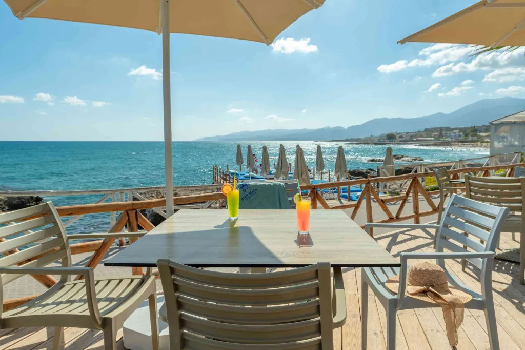 Une table avec des boissons est mise en scène sur une terrasse ensoleillée avec vue sur la mer.