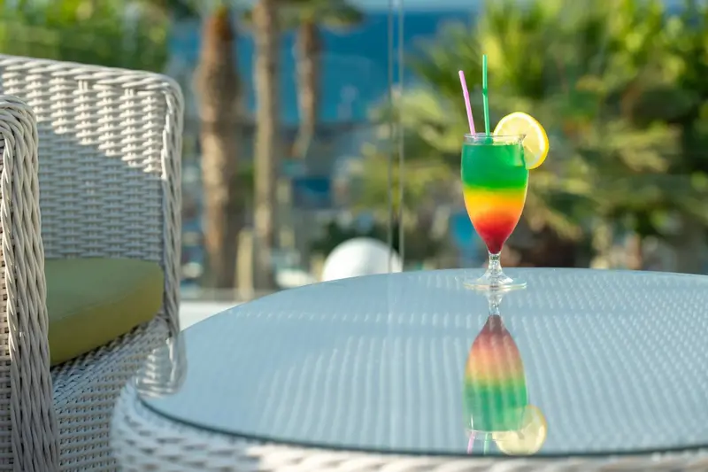 Un cocktail coloré se tient sur une table basse en verre, près d'un fauteuil en osier.