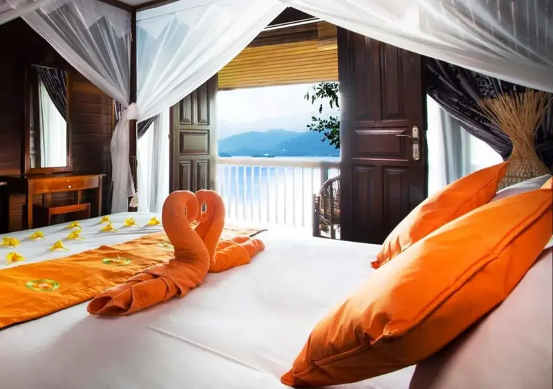 Une chambre lumineuse avec un lit décoré de serviettes en forme de cygnes, donnant sur une vue sur la mer.