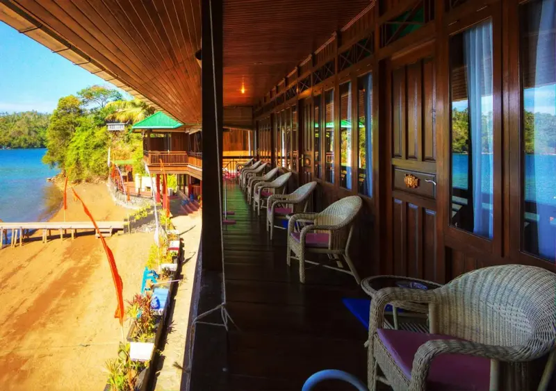 Terrasse en bois bordée de fauteuils donnant sur une plage de sable et la mer.