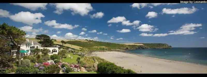 Vue d'une plage de sable fin bordée de collines verdoyantes et d'une résidence.