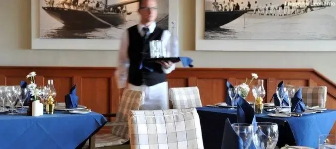 Une salle de restaurant lumineuse avec des tables dressées et un serveur.